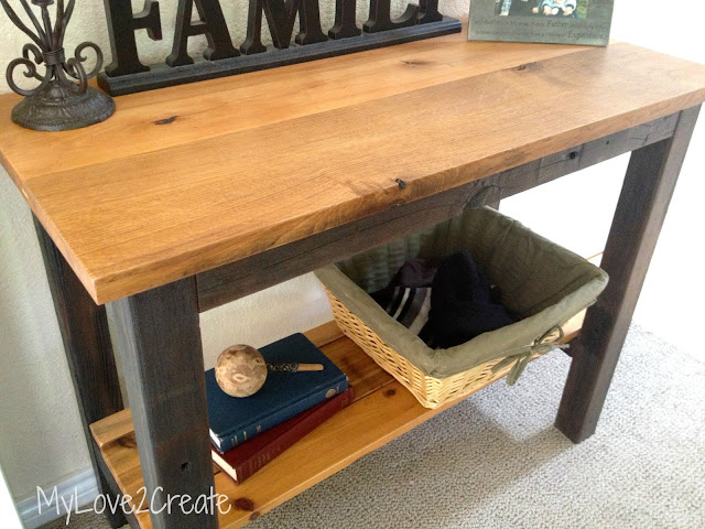 Rustic wooden console table with a natural wood top, dark-stained legs, and a lower shelf holding a wicker basket and decorative items.