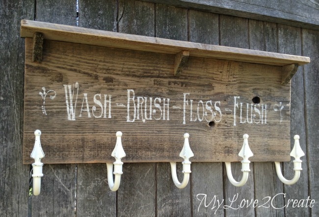 Rustic DIY towel rack made from reclaimed wood with repurposed curtain tie backs as hooks, featuring a stenciled bathroom reminder.