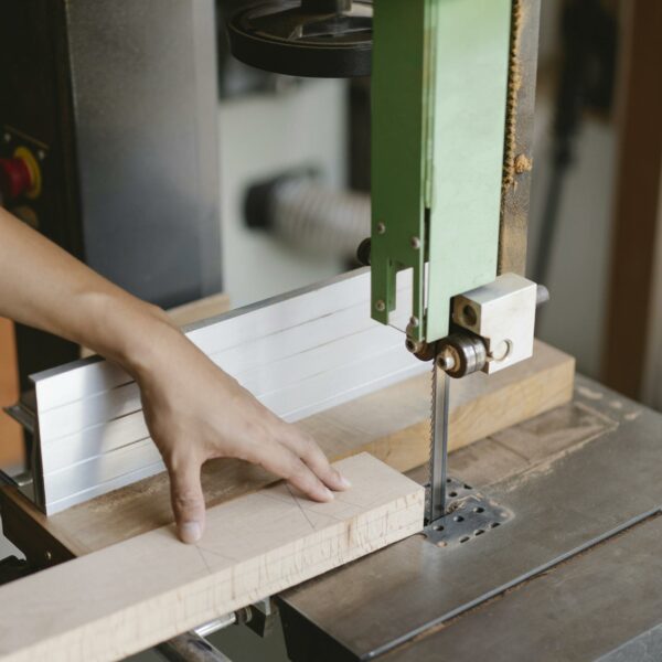 Crop unrecognizable woodworker sawing wooden plank with band saw with sharp blade in daytime