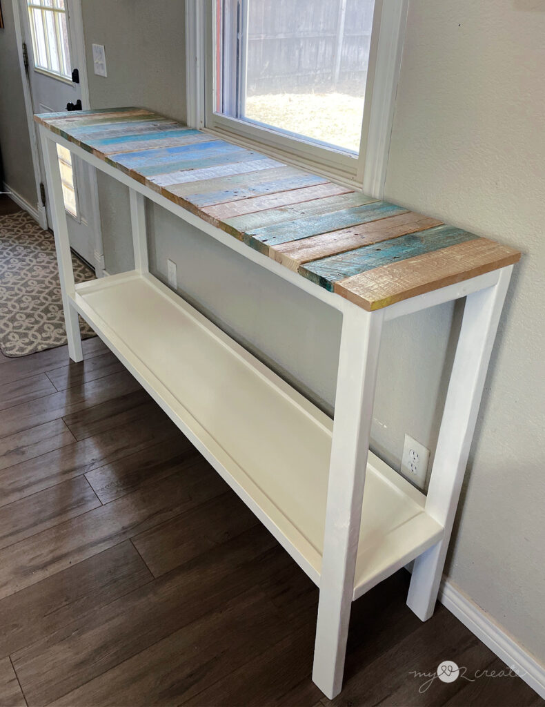 A completed DIY console table with a white painted frame and a colorful reclaimed wood top.