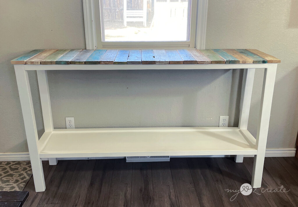 A completed DIY console table with a white painted frame and a colorful reclaimed wood top.