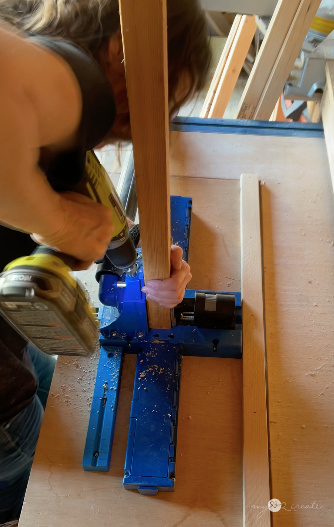 Woman drilling pocket holes into a wooden board using a blue Kreg jig on a workbench.