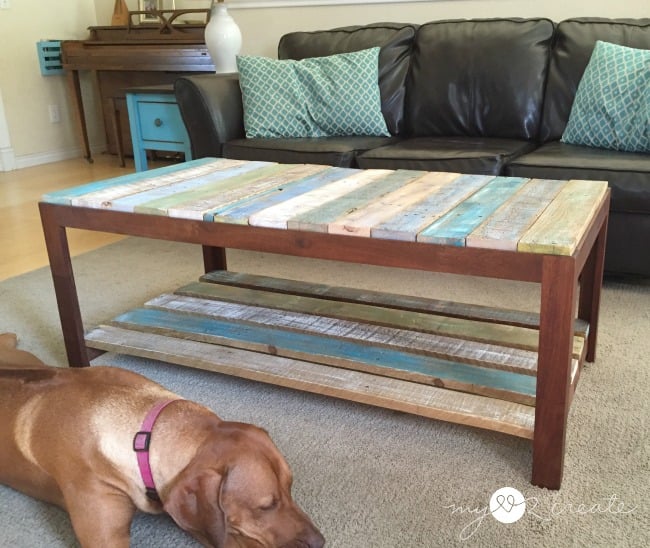 Rustic wooden coffee table with reclaimed wood slats in a cozy living room, featuring a black leather couch, a turquoise side table, and a resting brown dog