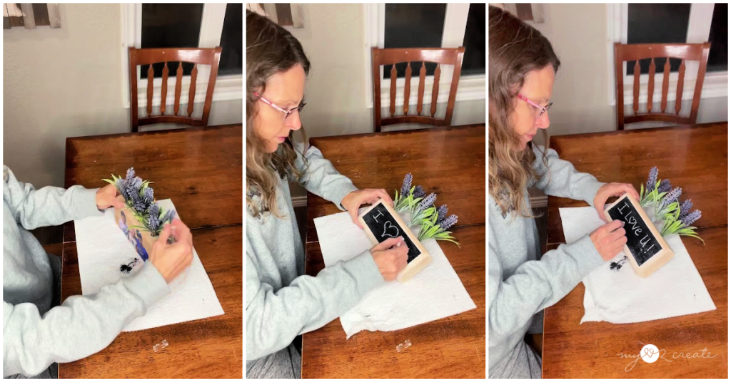 Woman decorating a DIY photo block with faux flowers and a chalkboard message that reads “I love U!”