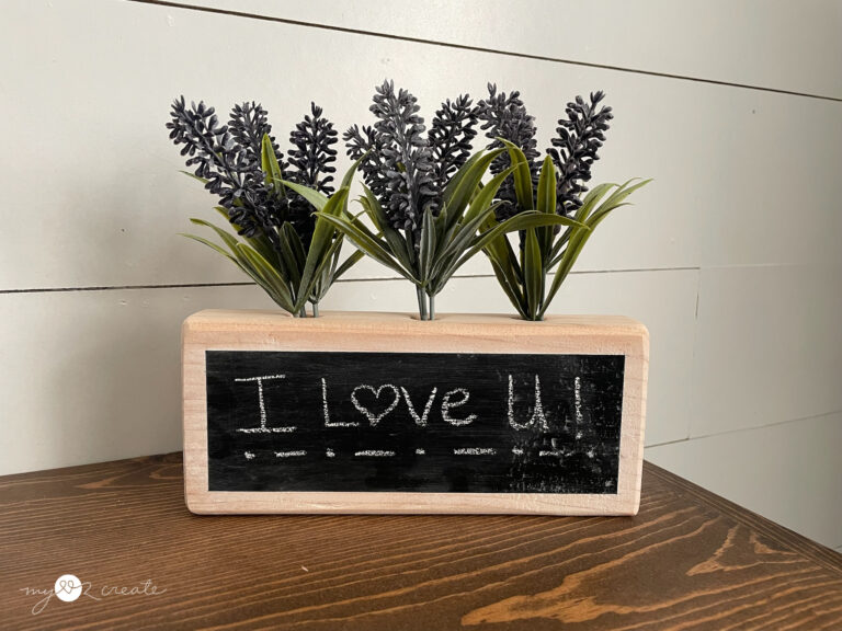 I Love U written on a wooden chalkboard with flowers on top of it
