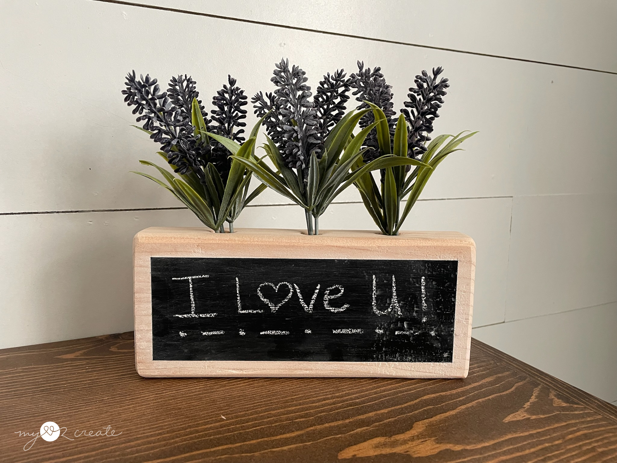I Love U written on a wooden chalkboard with flowers on top of it