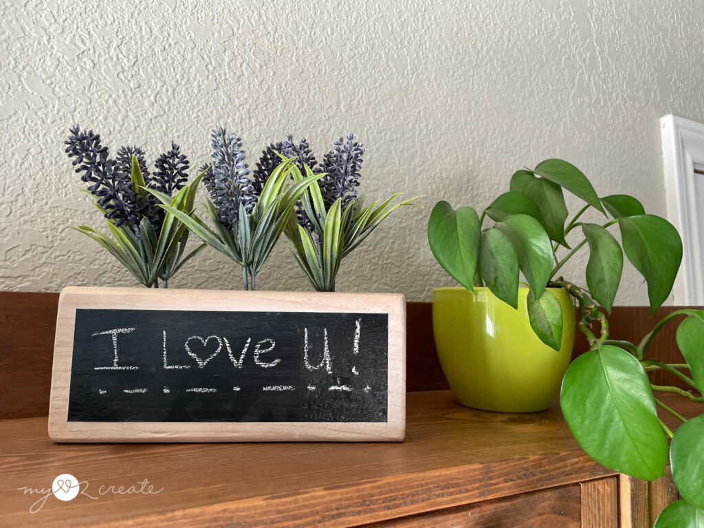 I Love U written on a wooden chalkboard with flowers on top of it